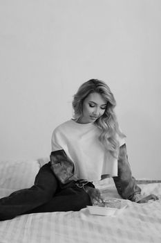 Fashionable woman relaxing on bed in a grayscale bedroom setting, smiling and seated.