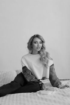 Stylish portrait of a woman with long hair sitting on a bed, captured in black and white.