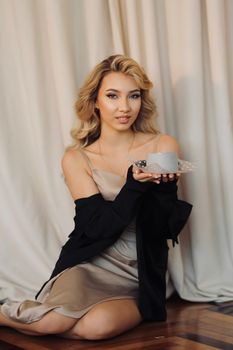Fashionable woman in a satin dress elegantly holding a cake indoors, showcasing style and poise.