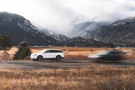 A white SUV drives along a scenic road in Colorado Springs, surrounded by stunning mountain views.