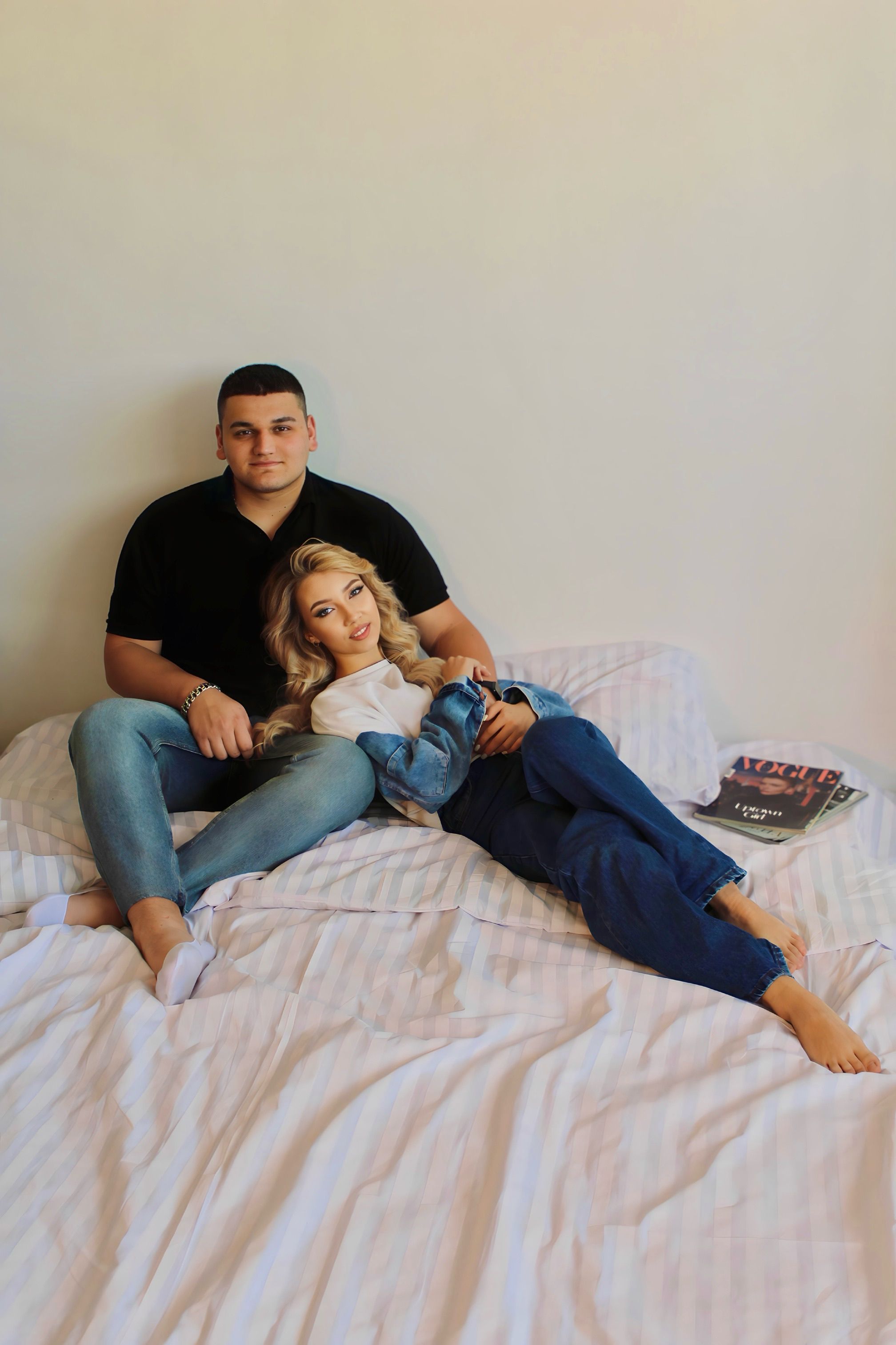 A young couple embraces while relaxing on their bed, creating a cozy and intimate setting.