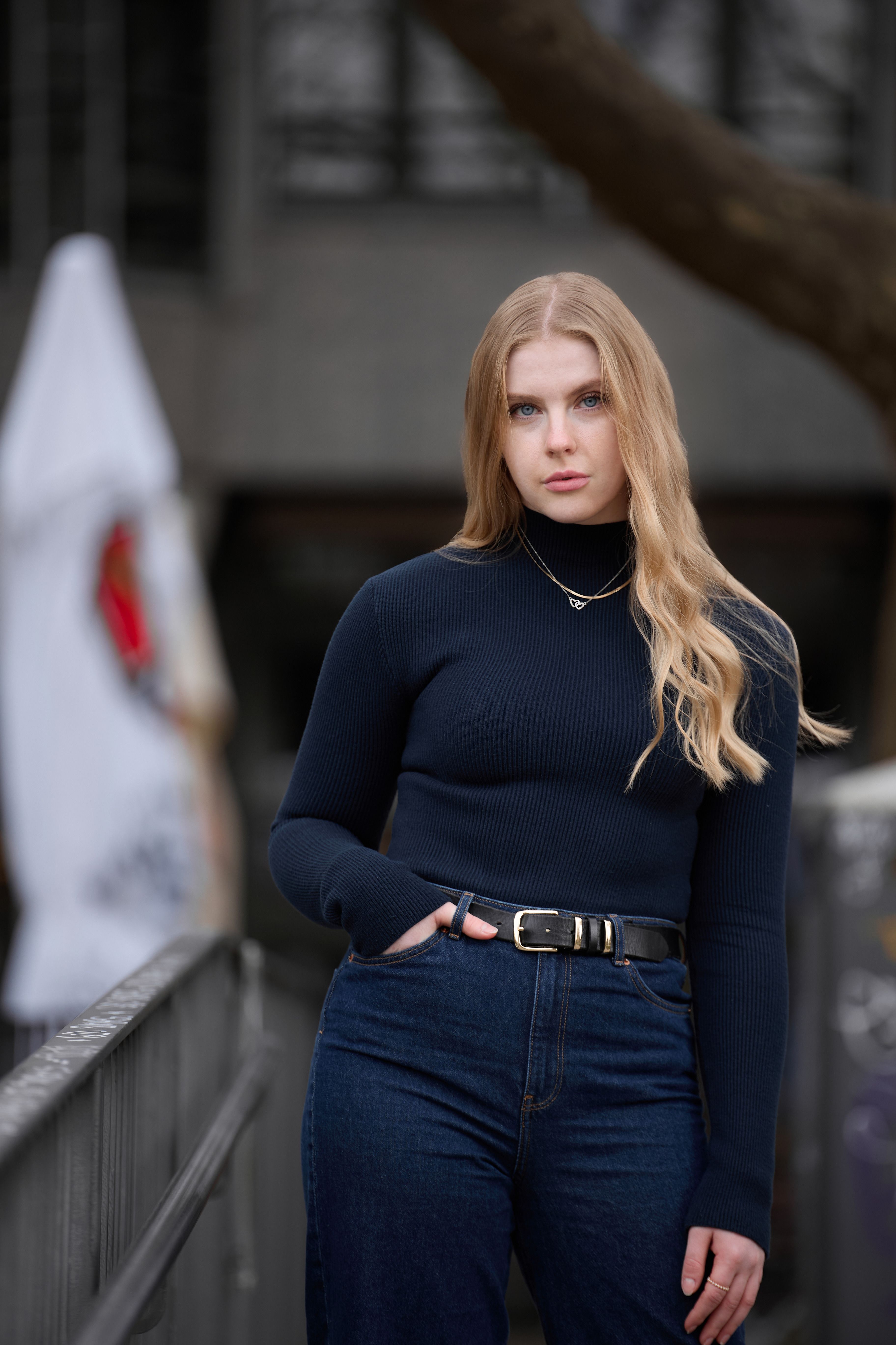 Stylish young woman in a black turtleneck and jeans, standing outdoors, posing fashionably.