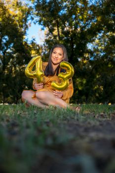 Woman with golden balloons celebrating 43rd birthday outdoors in a summer park.