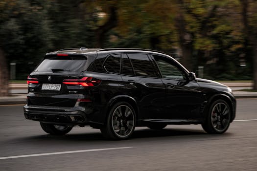 Black BMW X5 gracefully moves through city streets on a bright day.