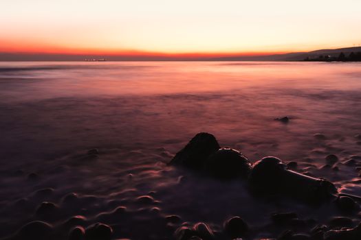 Peaceful sunset over a beach with smooth rocks in the foreground.