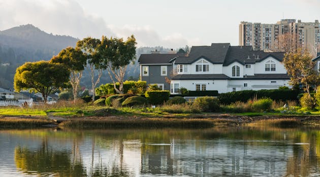 A peaceful suburban house by a serene lake with lush greenery and distant mountains.