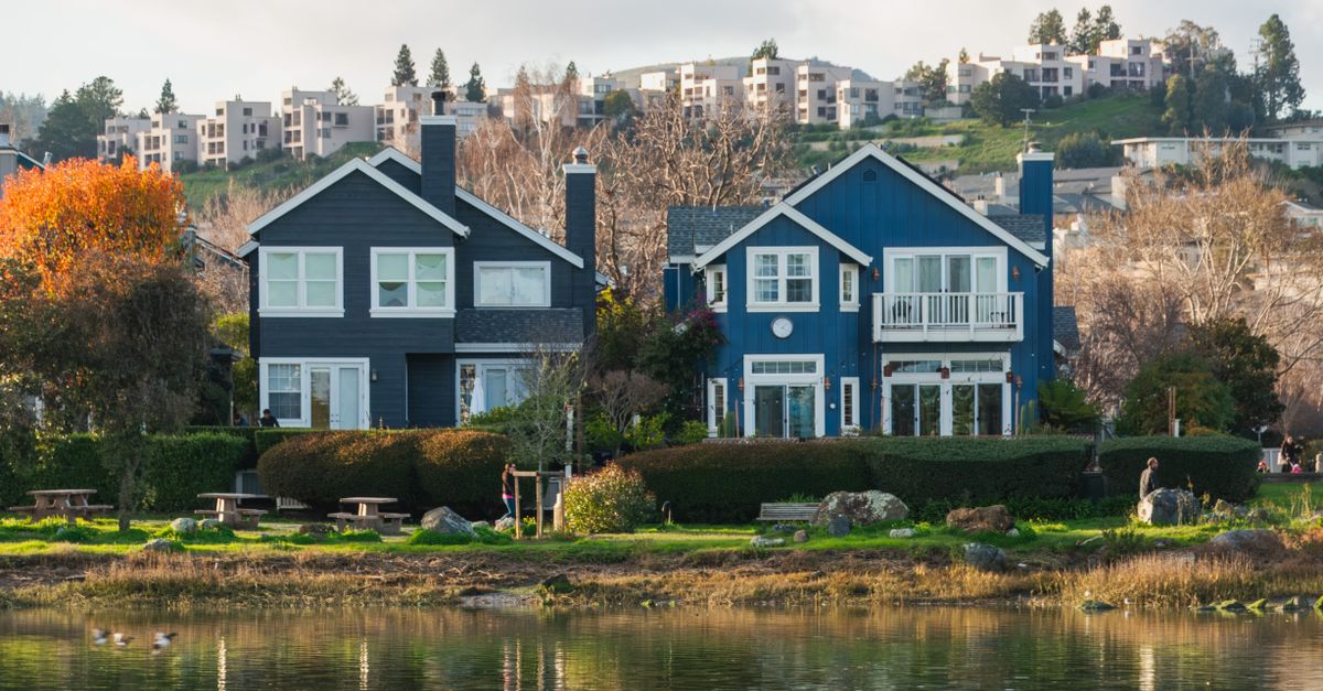 Beautiful row of waterfront homes surrounded by autumn trees reflecting in a calm river.