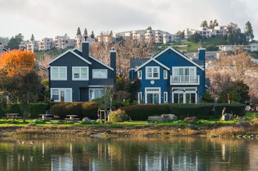 Beautiful row of waterfront homes surrounded by autumn trees reflecting in a calm river.