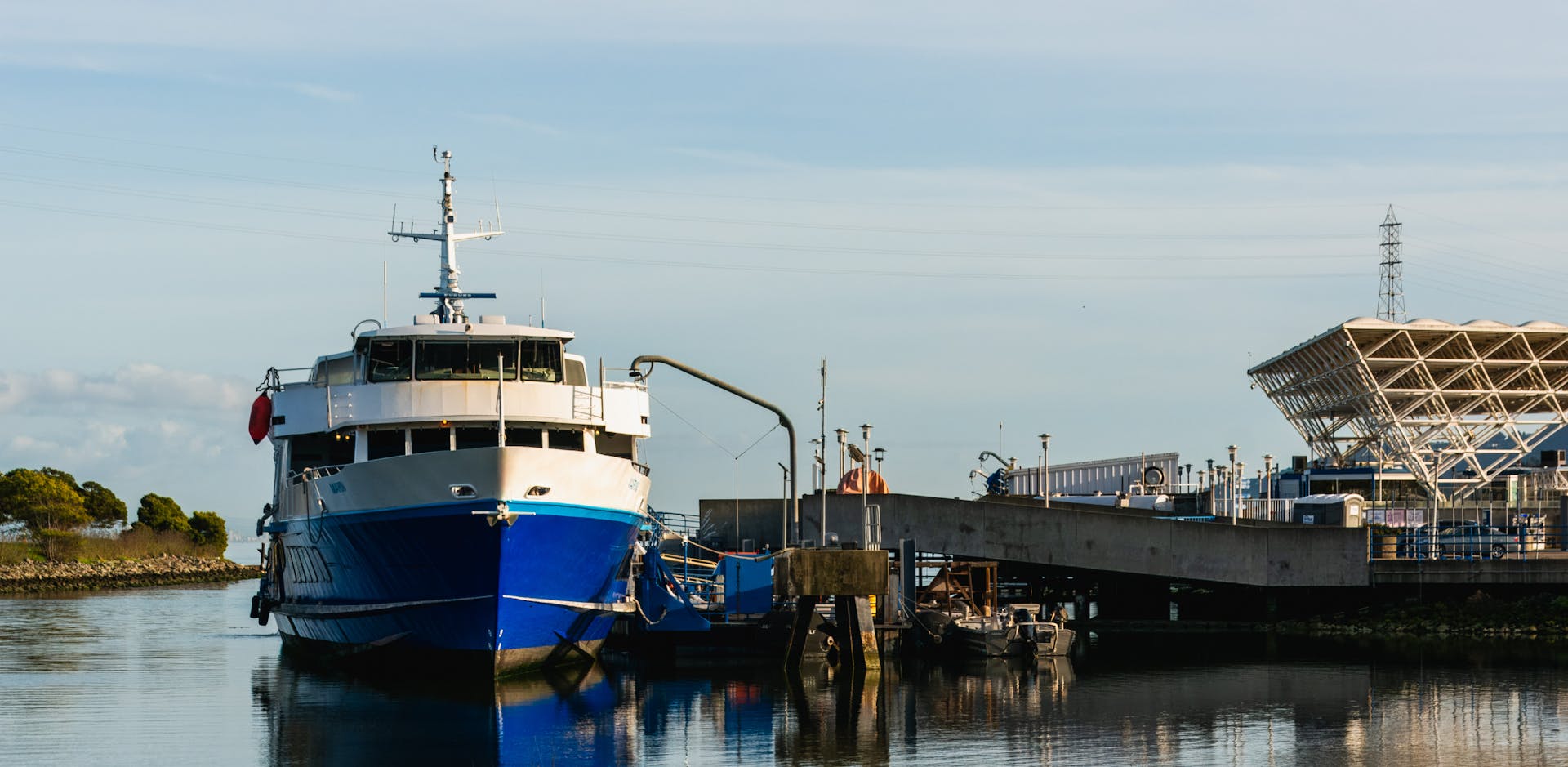 A large blue passenger ship docked at a modern harbor terminal during the day.