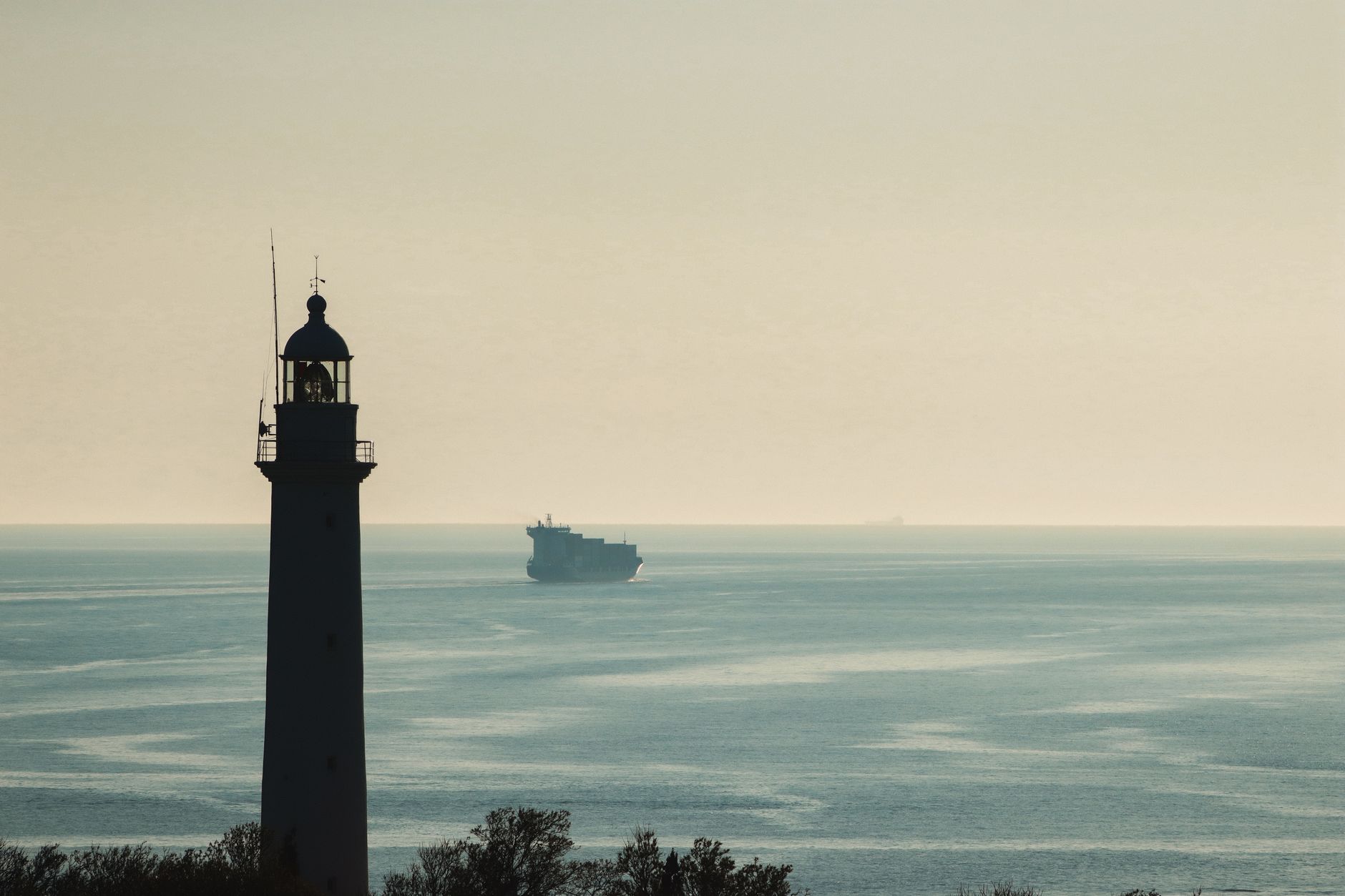 A serene view of a lighthouse against the Dardanelles Strait at Çanakkale, Türkiye, with a ship on the horizon.