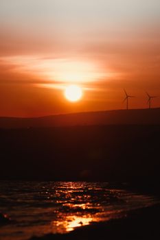 Vibrant sunset casting silhouettes on wind turbines and sea at Şarköy, Türkiye.