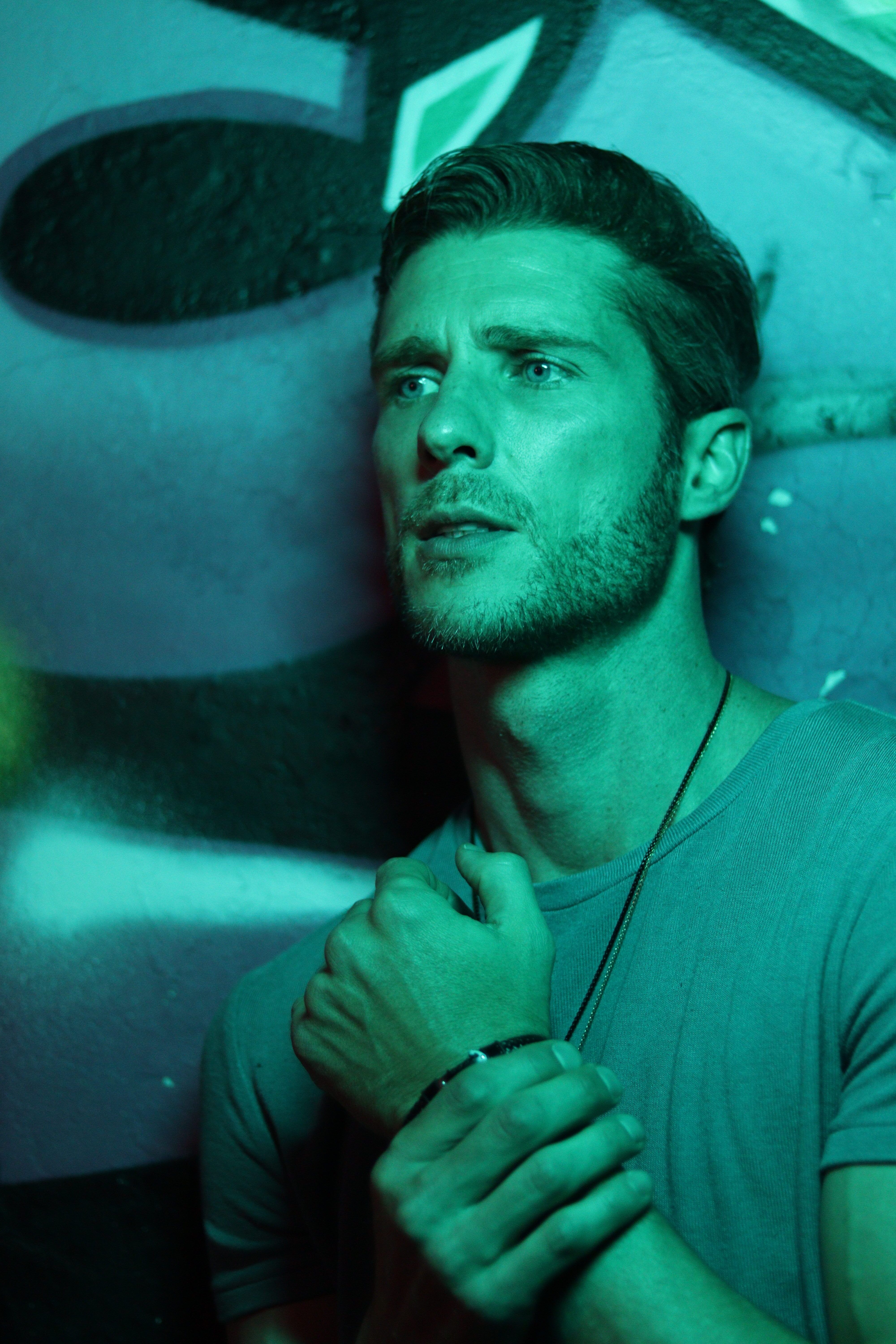 A contemplative man poses under green neon light, creating a moody portrait.