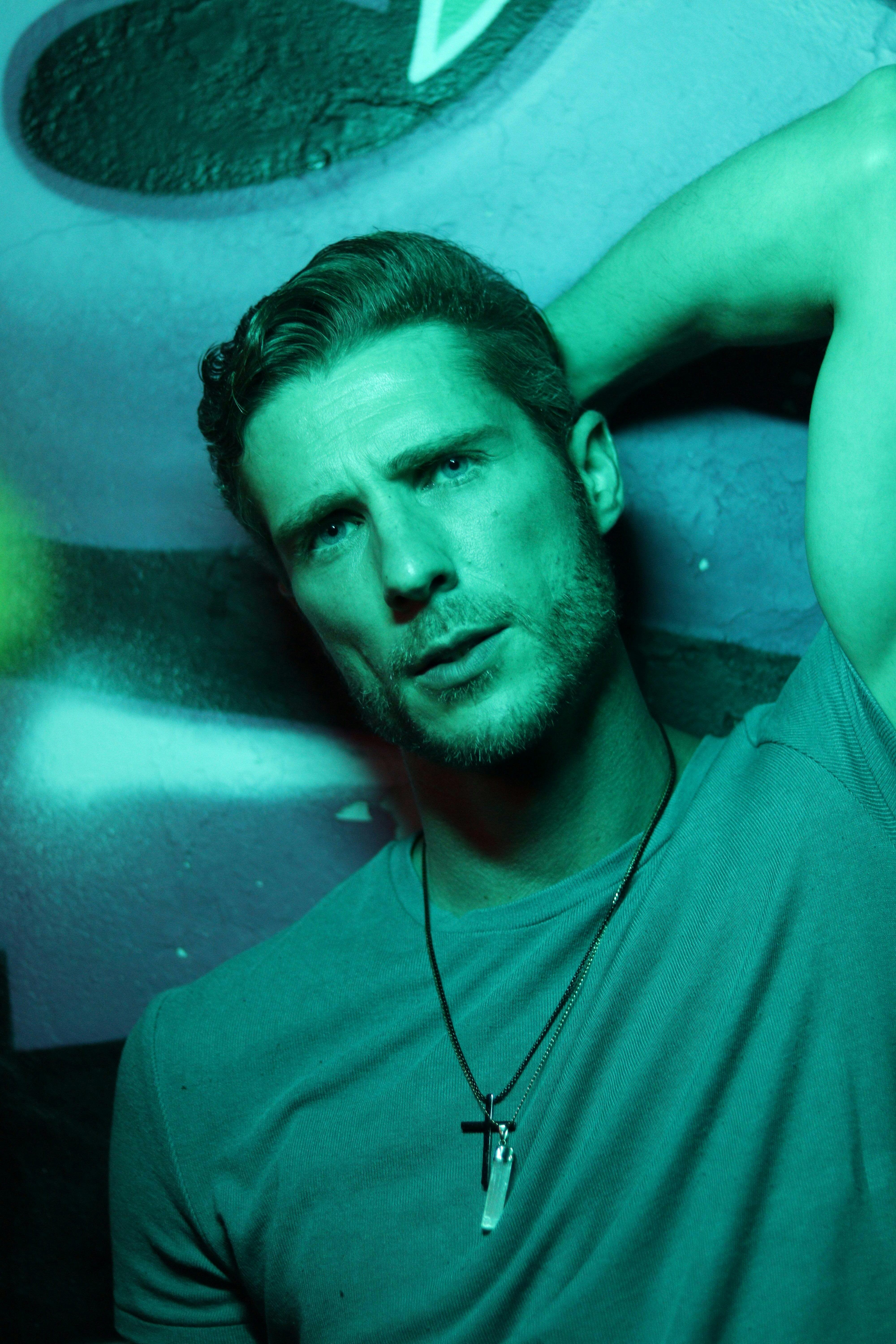 Striking portrait of a man in a green light with a contemplative pose and necklace.