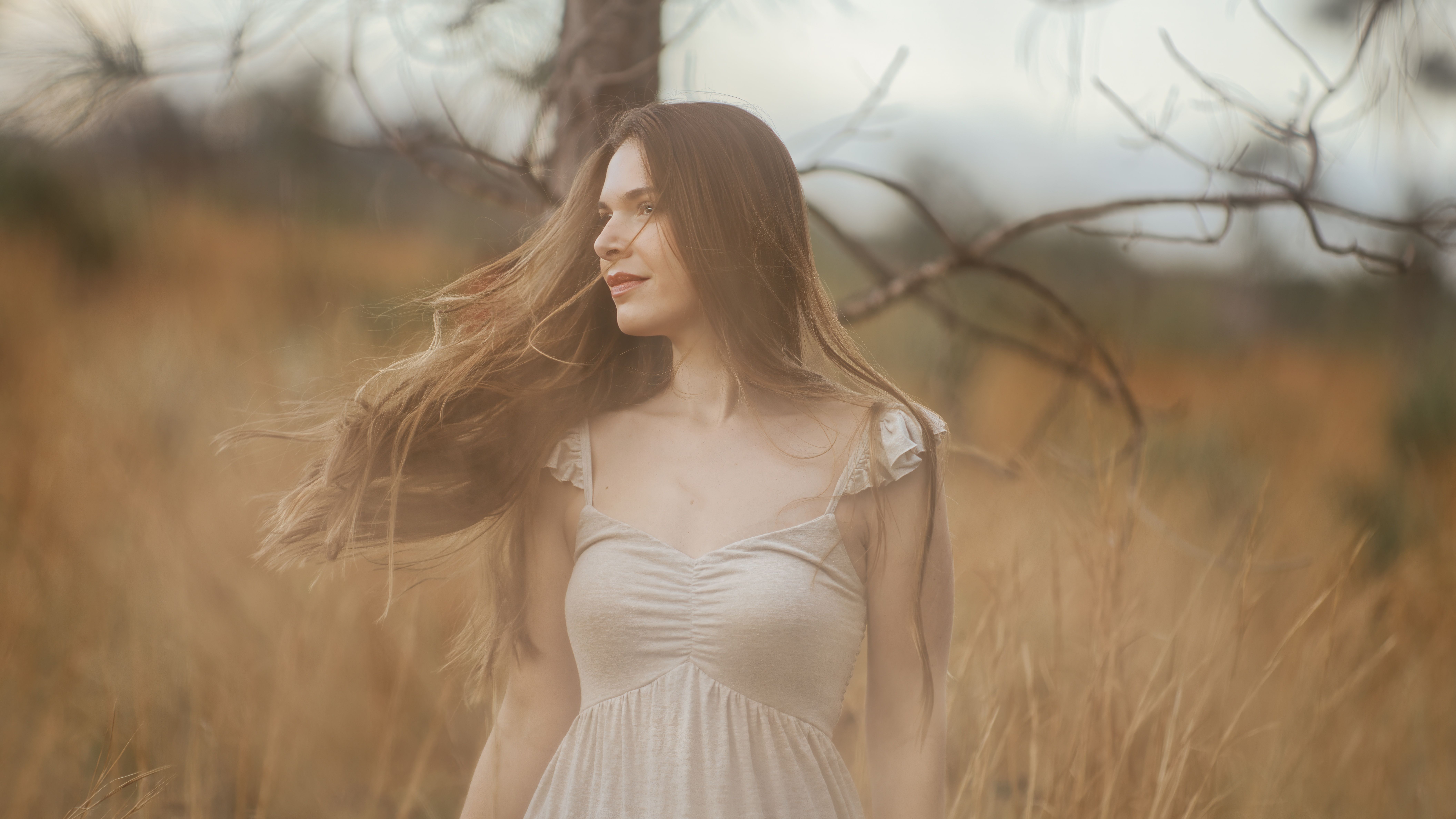 Elegant woman with flowing hair in a tranquil rural field, evoking a serene and natural atmosphere.
