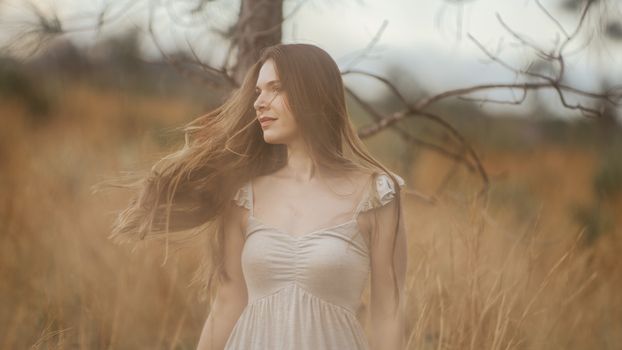 Elegant woman with flowing hair in a tranquil rural field, evoking a serene and natural atmosphere.