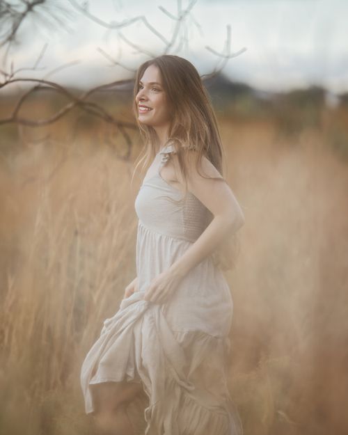 Free Elegant woman with long hair smiling in a serene field landscape during the day. Stock Photo