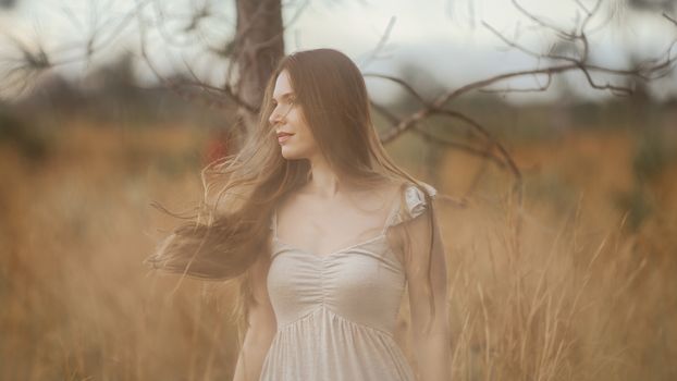 A woman in a white dress enjoys the calm of a rural field.