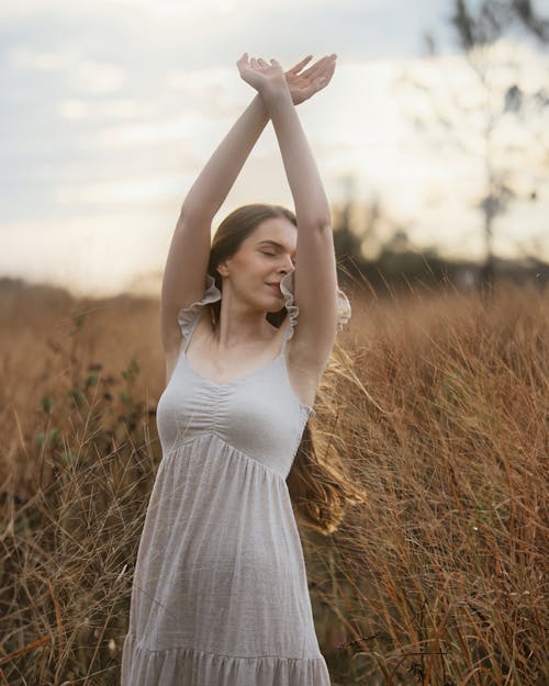 Woman in White Dress Standing with Arms Raised on Field