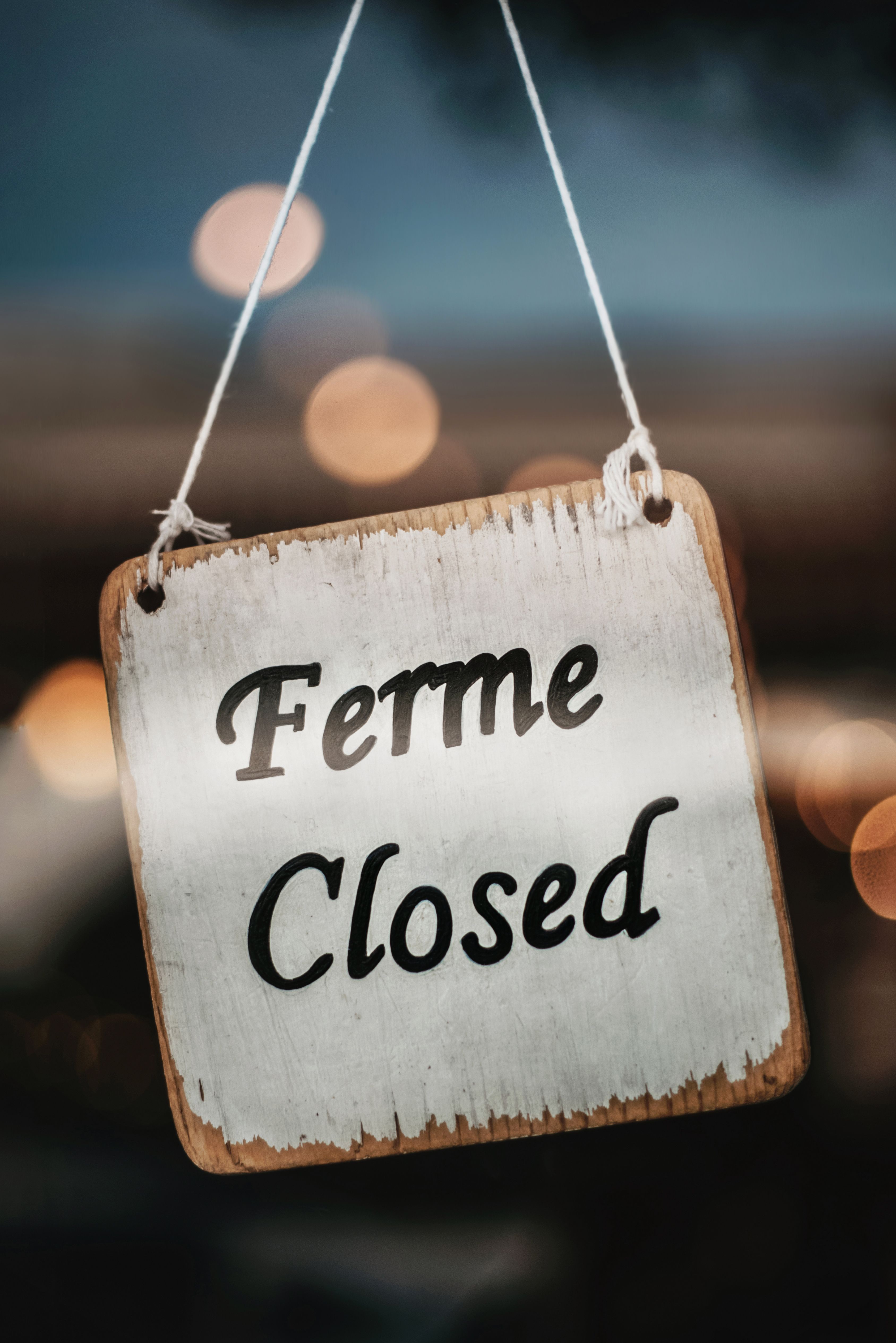 A close-up of a wooden sign reading 'Ferme Closed' with a blurred background.