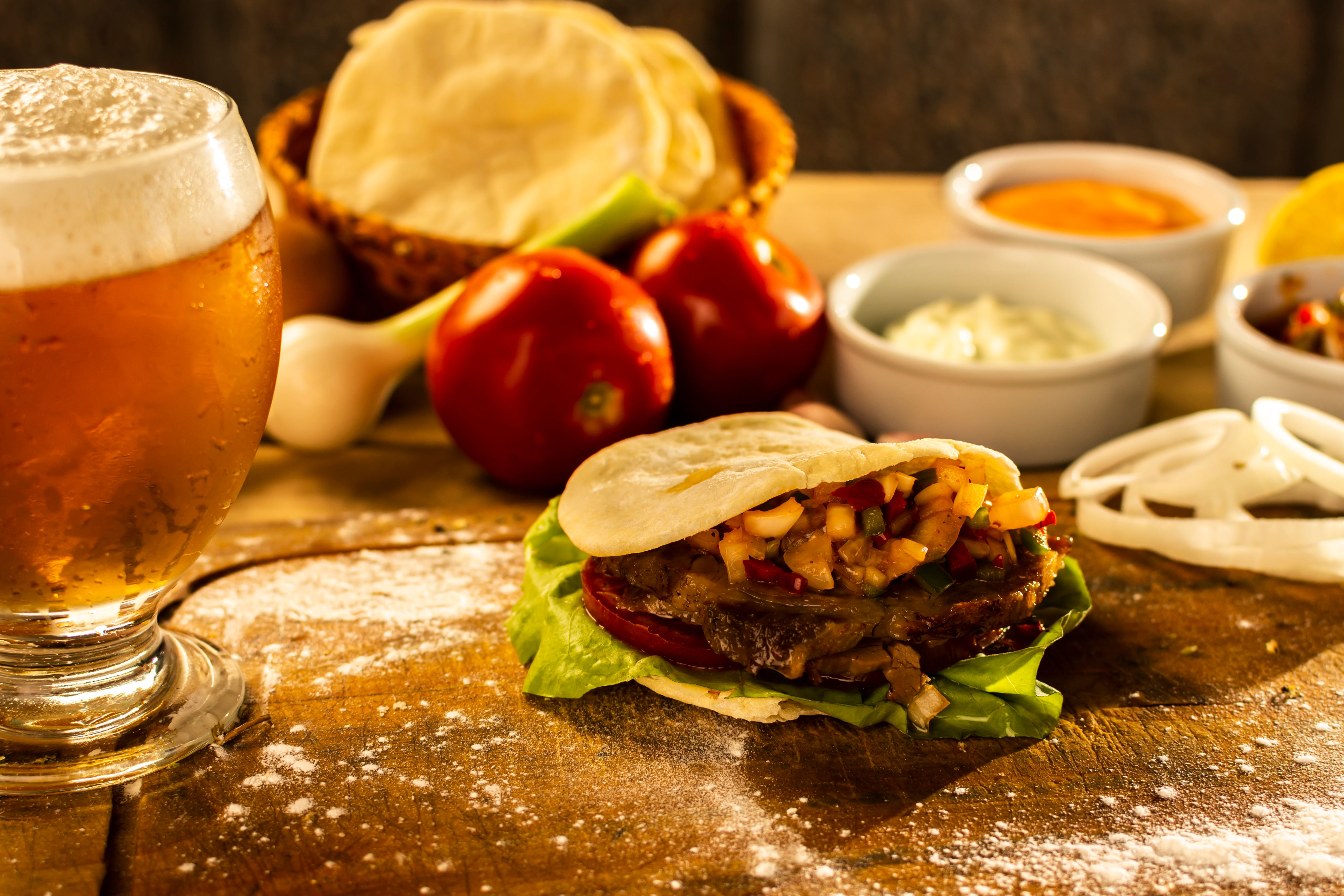 A tasty pita sandwich with fresh toppings paired with a glass of beer set on a rustic table.
