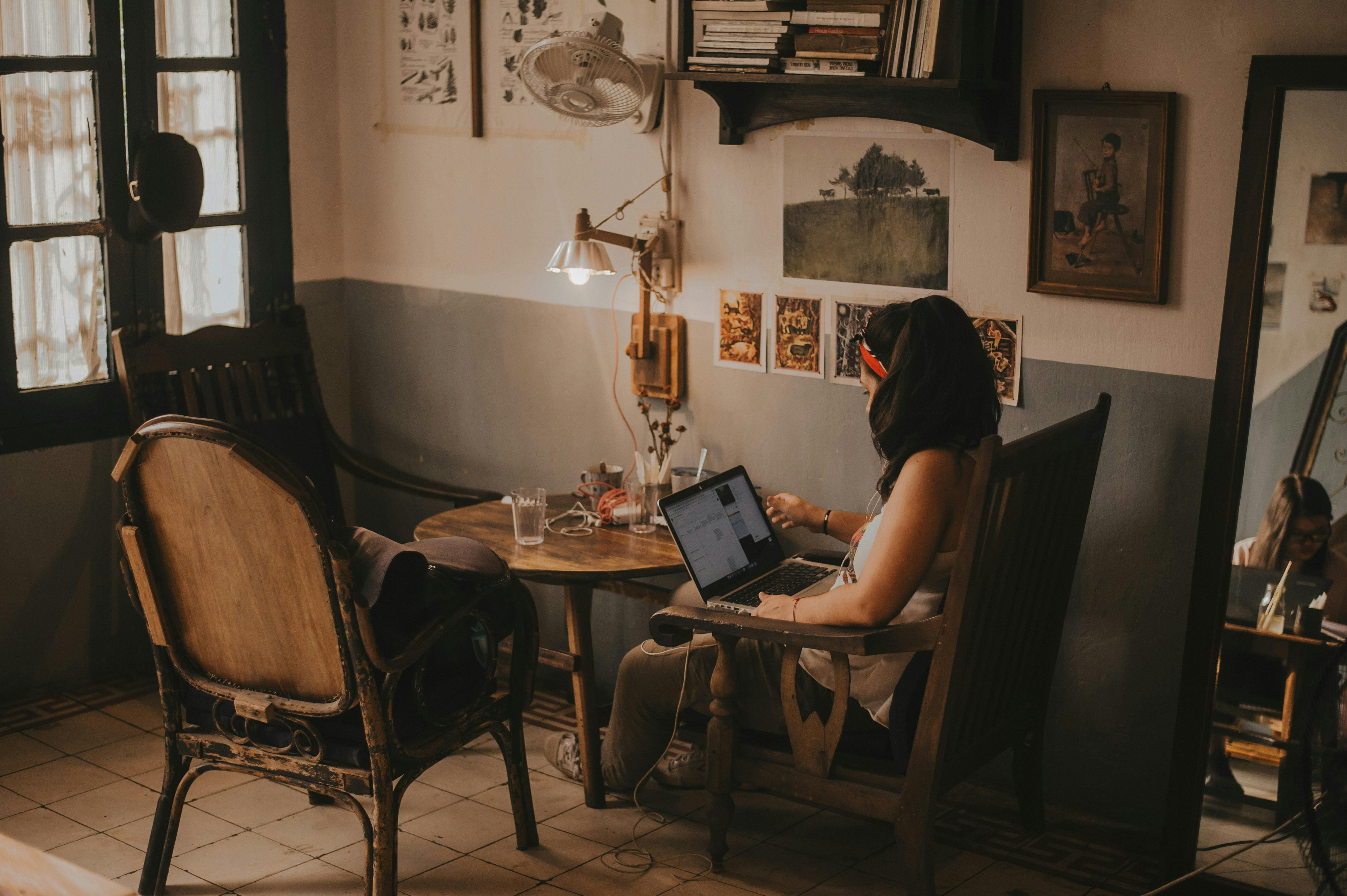 A woman working on a laptop in a cozy, vintage-style room with warm decor.