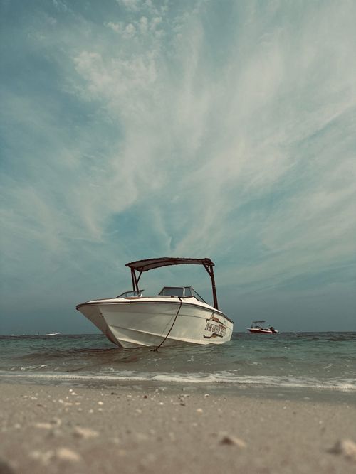 Free Motorboat anchored on a sandy beach under a vast cloudy sky, perfect for aquatic adventures. Stock Photo