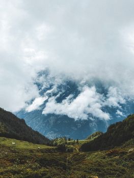 Serene mountain landscape with clouds covering peaks, lush greenery in foreground.