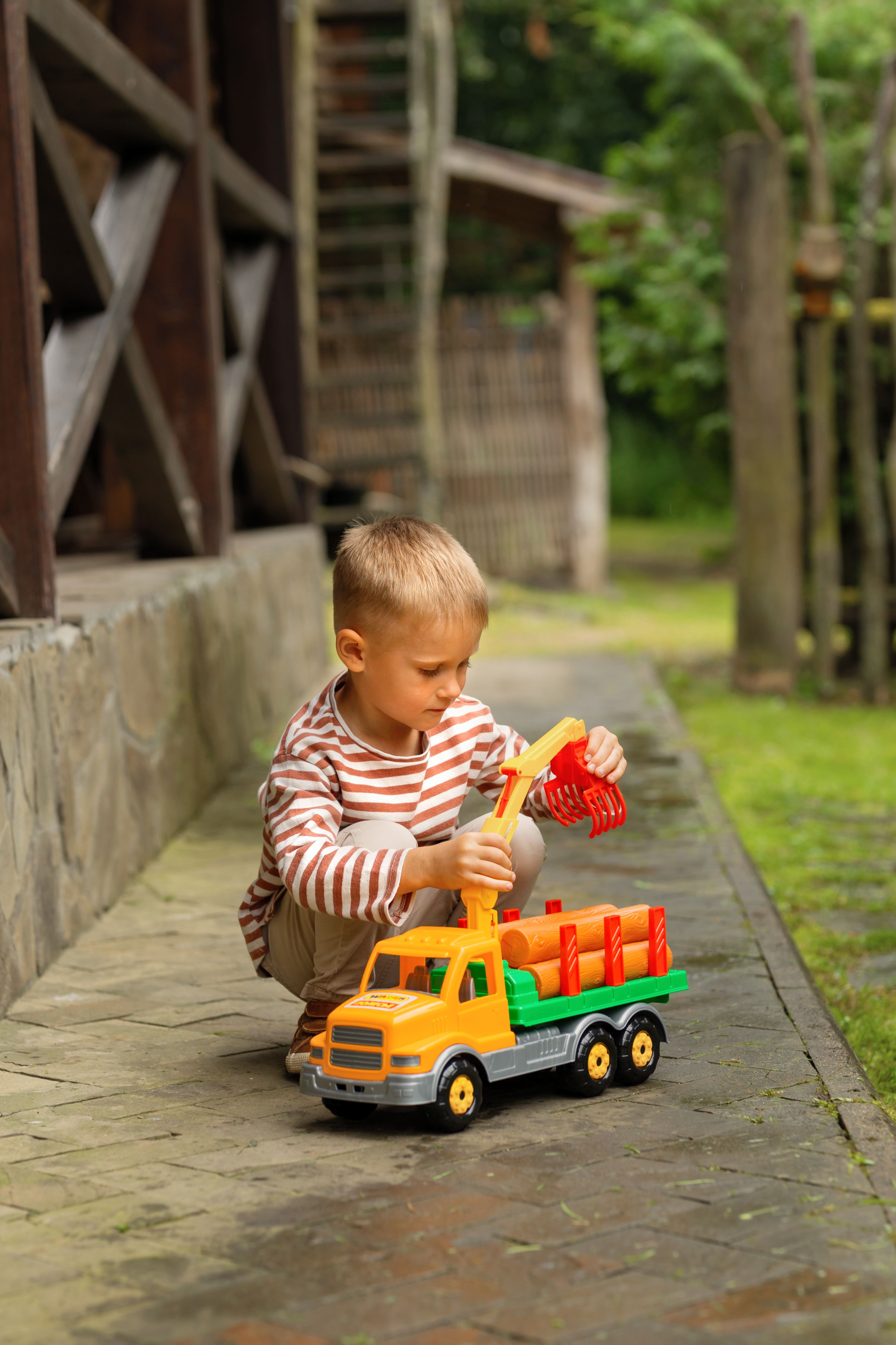 A young boy focused on playing with a brightly colored toy truck outdoors in warm weather.