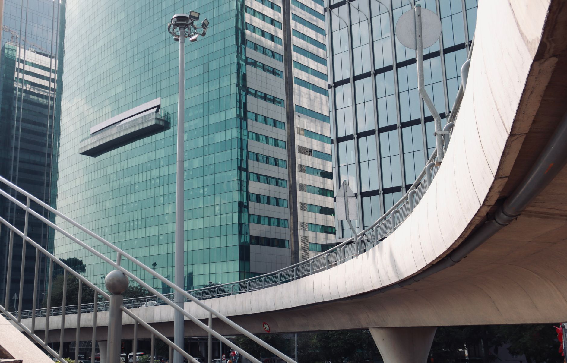 High-angle view of urban skyscrapers with reflective glass facades and curving viaduct in daylight.