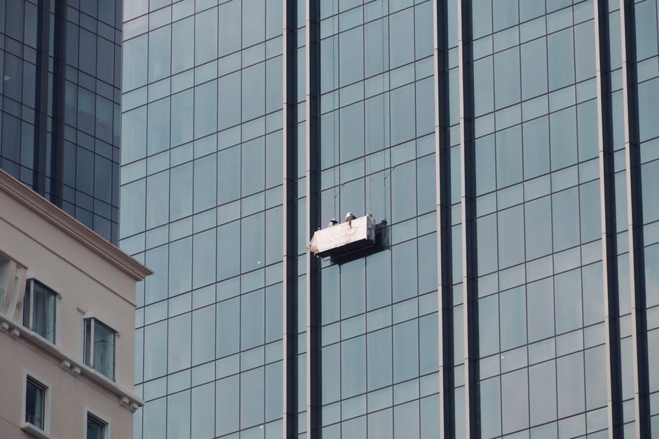 Two workers cleaning skyscraper windows on a suspended platform in an urban setting.