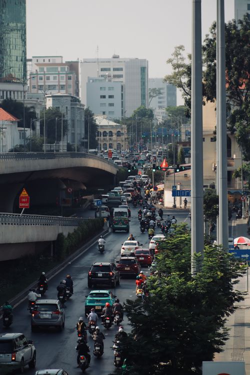 Free A vibrant city scene with bustling traffic including motor scooters and cars under an overpass. Stock Photo