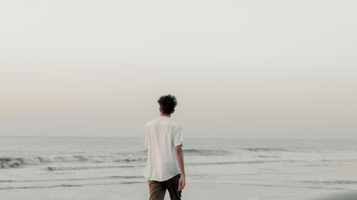 Free A man in a white shirt walks along a peaceful beach at dusk, embracing solitude. Stock Photo