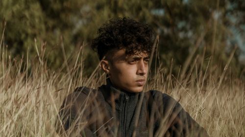 Free A young man with curly hair sitting pensively in a serene grassland setting. Stock Photo