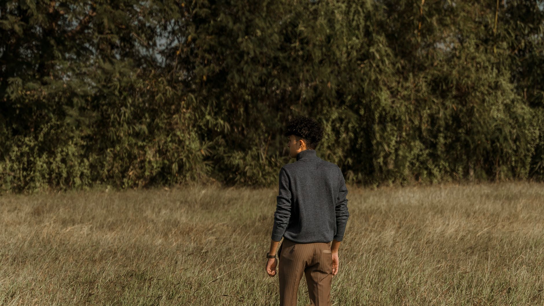 A man in stylish attire walking through tranquil grassland on a sunny day. Ideal for lifestyle themes.