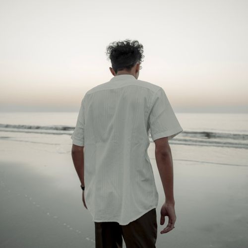 Free A man walks along a serene beach shore during twilight, wearing a white shirt. Stock Photo
