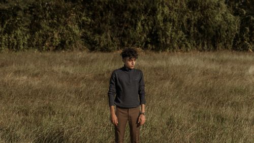Free Fashionable young man standing alone in a tranquil grassland, exuding a sense of calm and style. Stock Photo