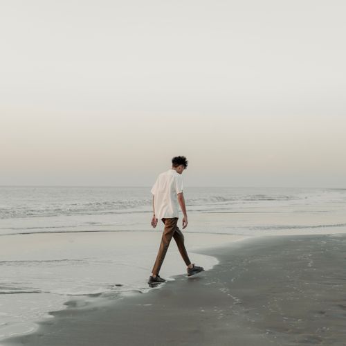 Free A man leisurely walks along a serene beach during sunrise, creating a peaceful scene. Stock Photo