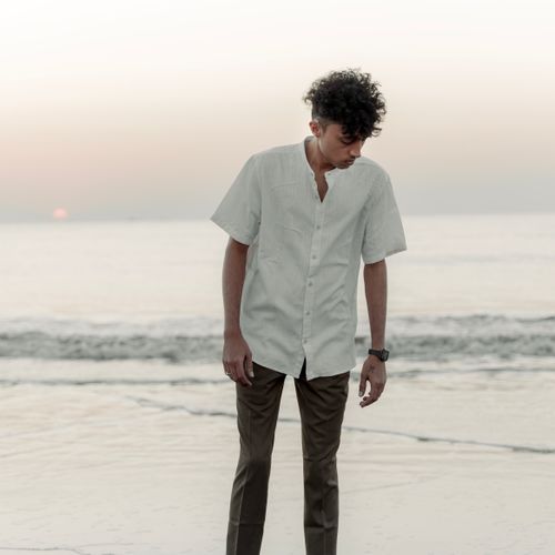 Free A young man stands on the beach in a white shirt during a serene sunset, lost in thought. Stock Photo