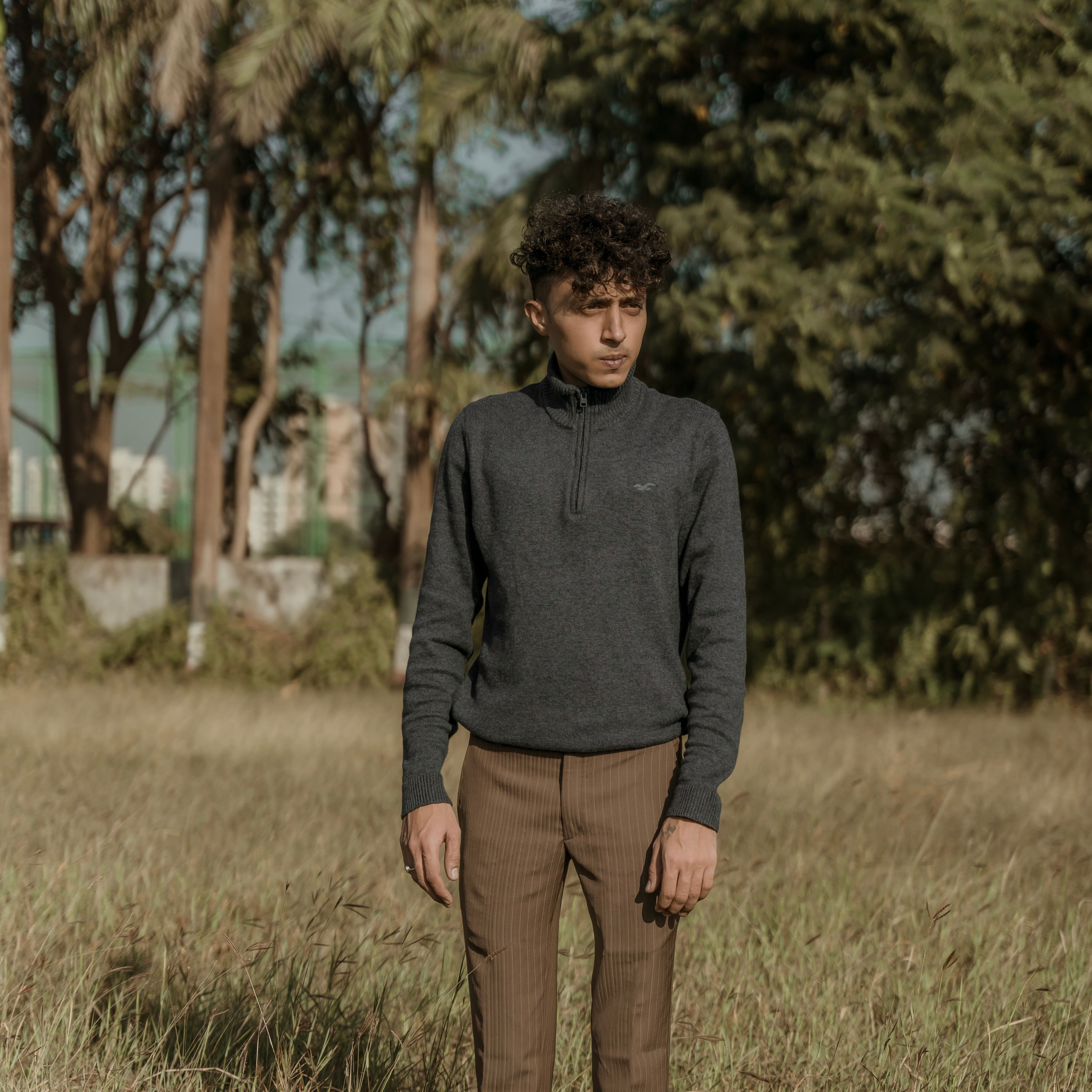 A young man stands in a grassy field under natural light, epitomizing rugged fashion.