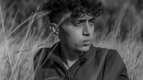 Free Artistic black and white portrait of a young man sitting amidst tall grasses. Stock Photo