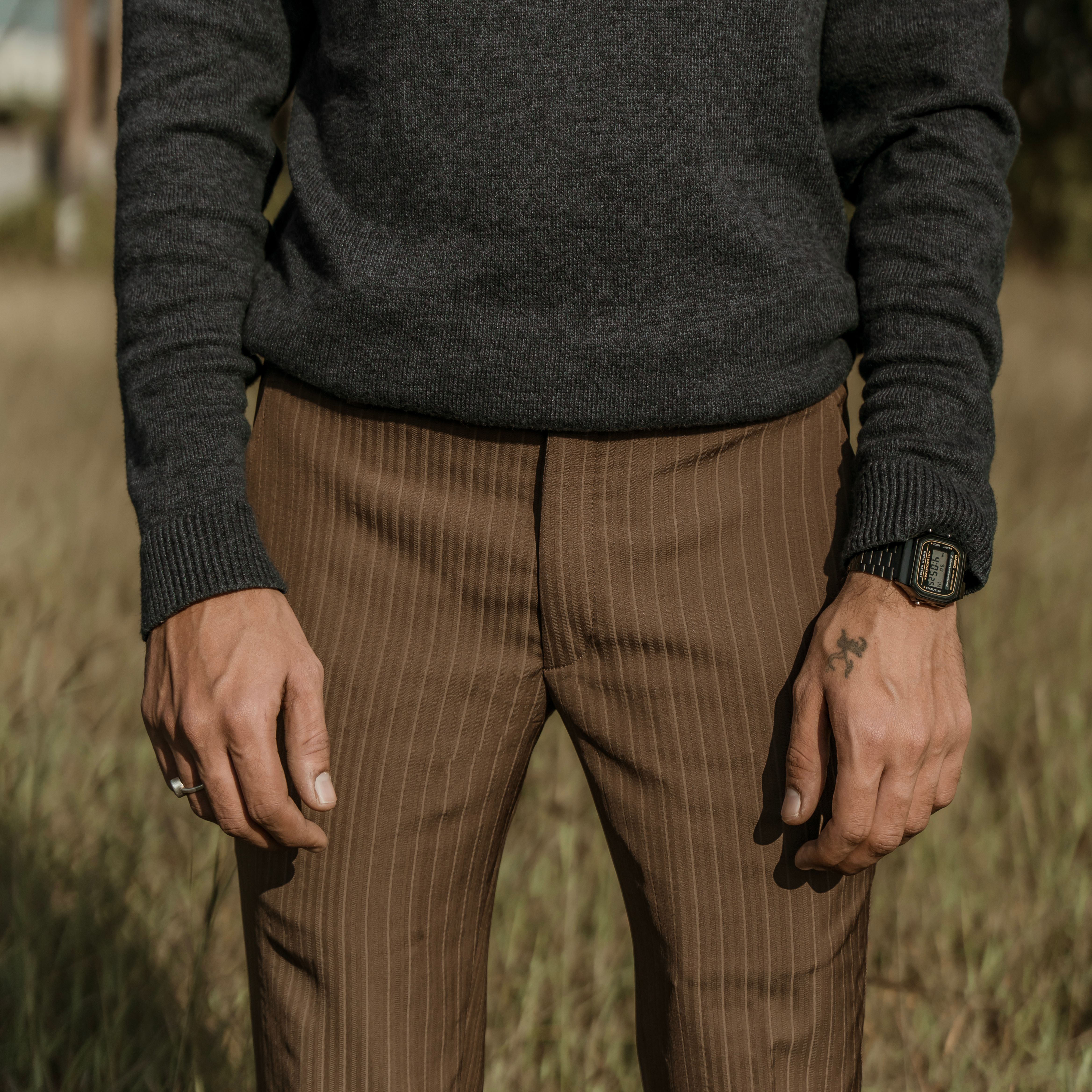 Man's fashion shoot outdoors featuring brown pinstripe pants and a gray sweater with accessory focus.