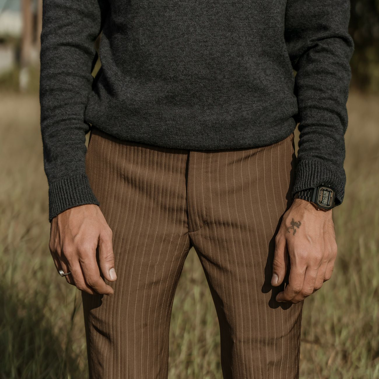 Man's fashion shoot outdoors featuring brown pinstripe pants and a gray sweater with accessory focus.