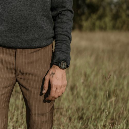 Free A person wearing a sweater and watch with a tattoo stands in a grass field. Stock Photo
