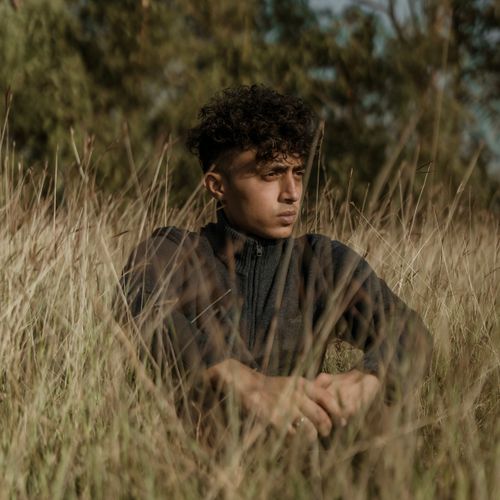 Free A young man with curly hair in a zipper sweater poses contemplatively outdoors. Stock Photo