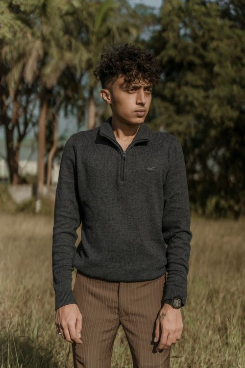Free Man posing outdoors in gray pullover and brown pants, showcasing curly hair fashion style. Stock Photo