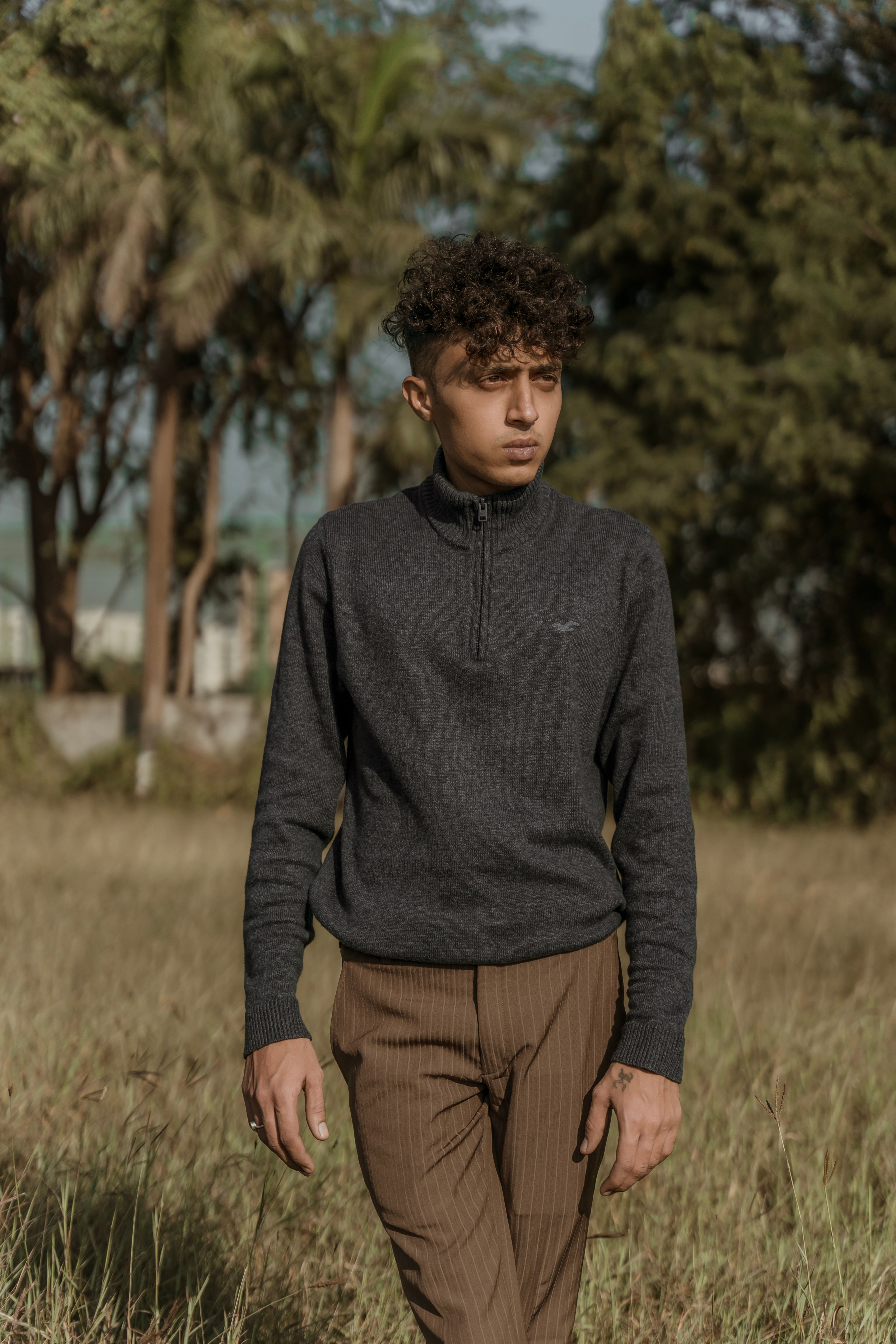 Man with curly hair and brown pants posing outdoors in autumn fashion.