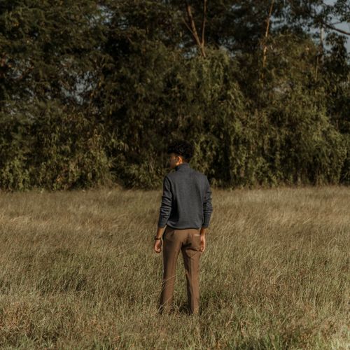 Free A man standing in a grassy meadow surrounded by trees, facing away, in a rural setting. Stock Photo