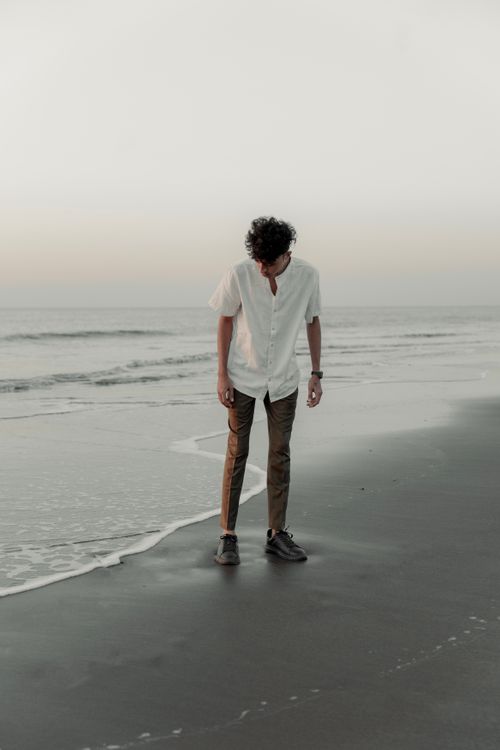 Free Young man in white shirt walking on a peaceful beach at sunset, reflecting serenity. Stock Photo