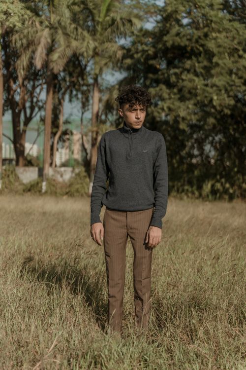 Free A young man stands in a grassland dressed in modern fashion, surrounded by trees. Stock Photo