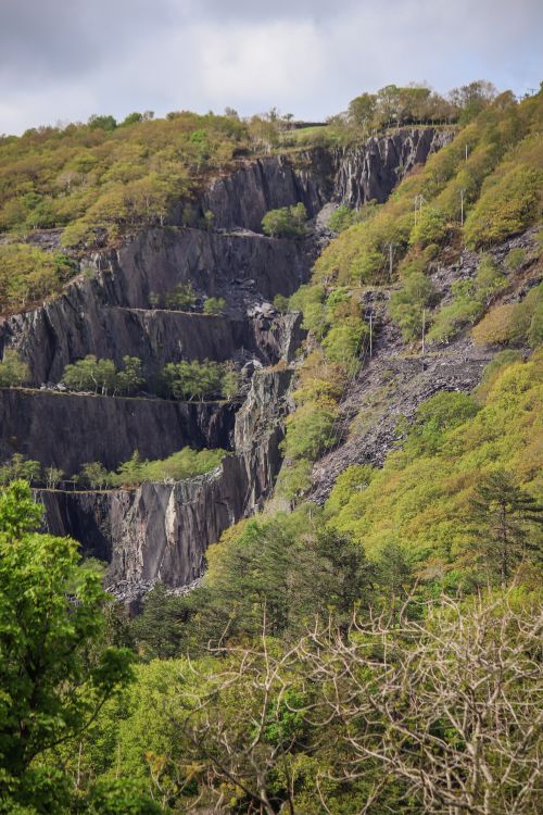 Free Aerial view of a verdant hillside with rocky formations and dense forests under a cloudy sky. Stock Photo